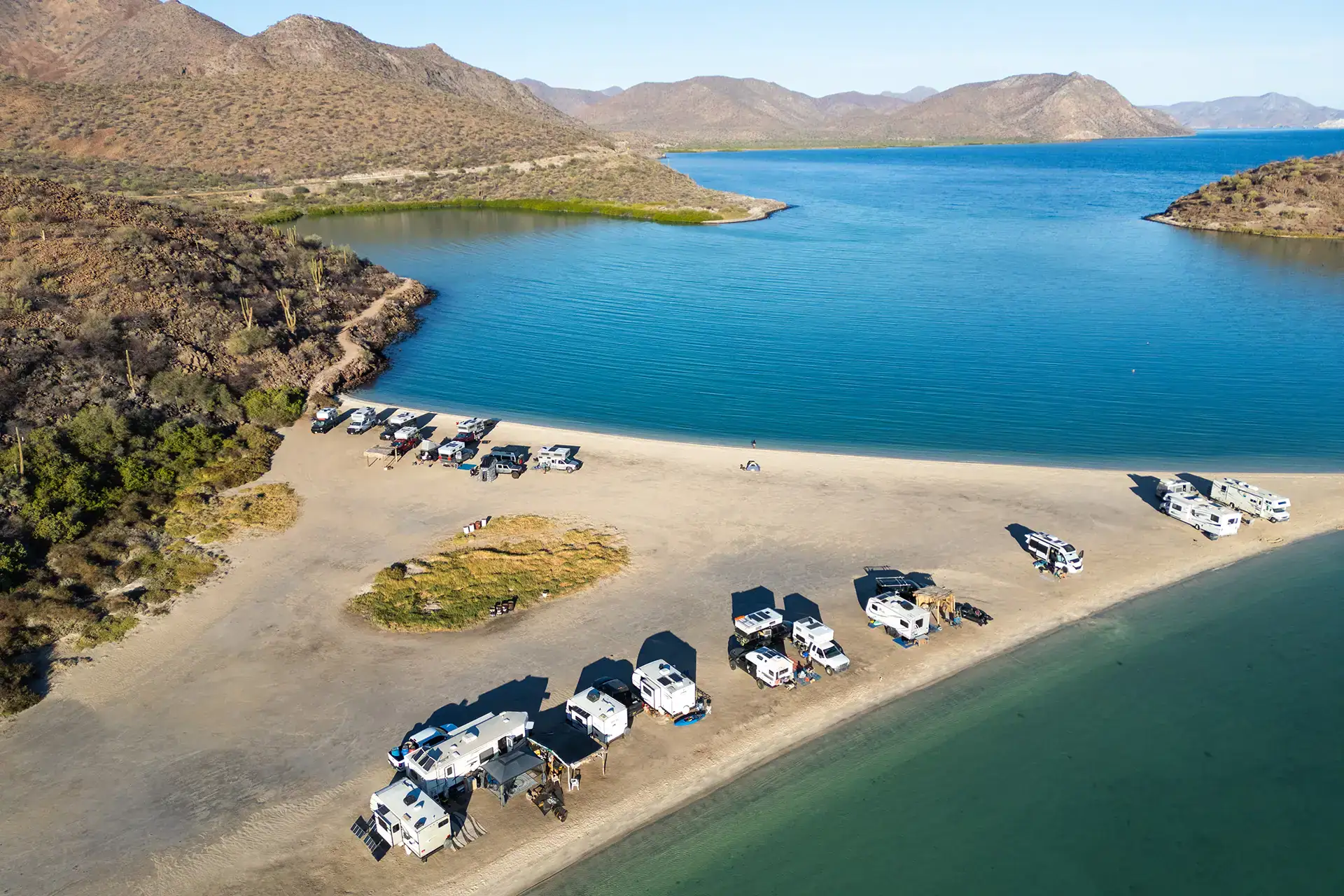Campers and RVs parked on beach for off-grid boondocking, overlanding adventure by turquoise waters.