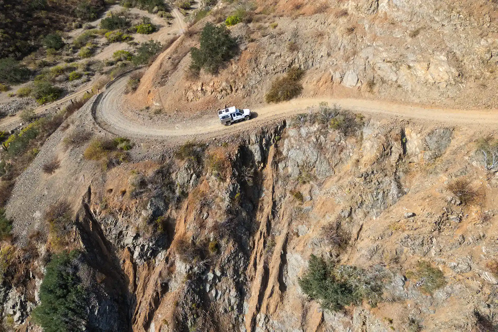 White Four Wheel Camper truck navigating dusty remote overlanding road, off-grid boondocking adventure.