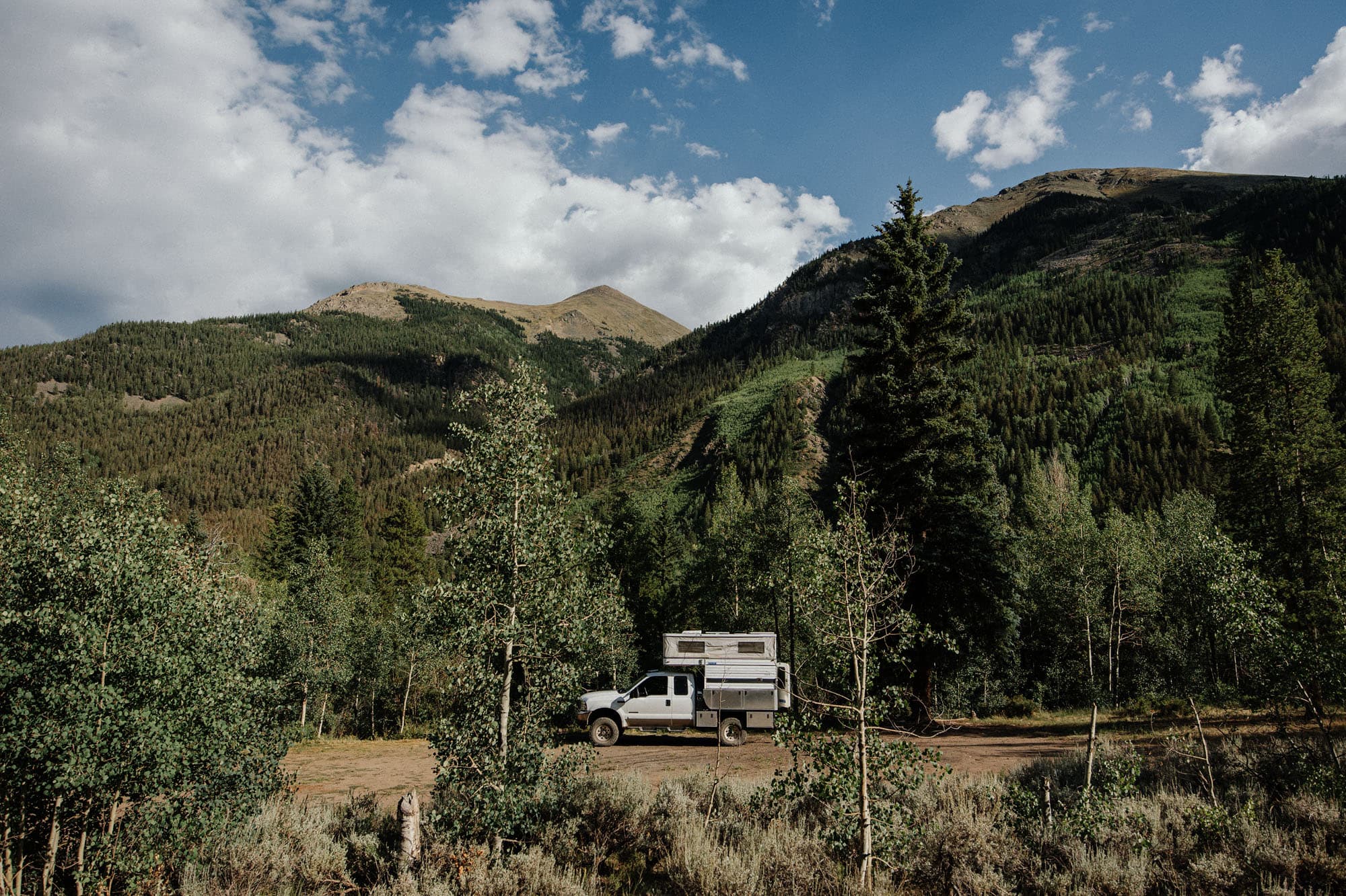 White Four Wheel Camper truck boondocking off-grid, overlanding in forested mountain landscape.