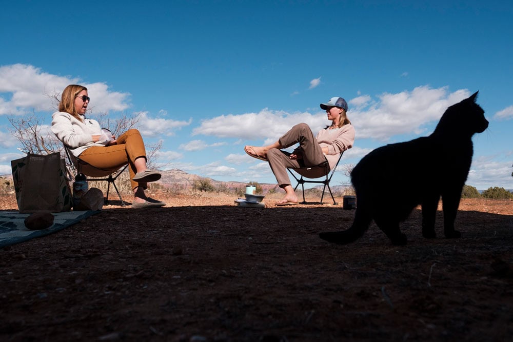 Two people relaxing outdoors while black cat silhouetted in foreground, boondocking setting