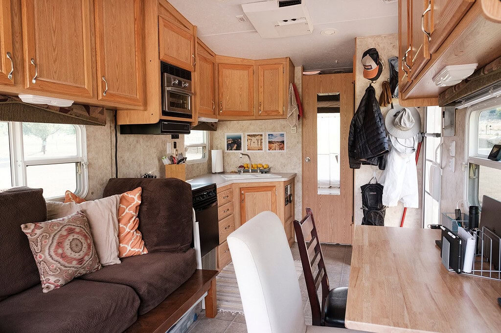 Cozy Four Wheel Camper interior with brown sofa, kitchen, desk, and apparel for off-grid boondocking overlanding.