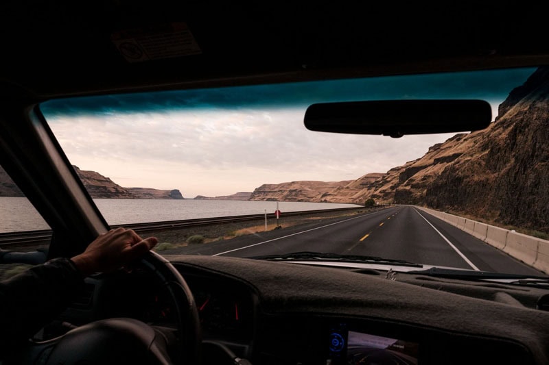 Driver's hand on wheel, scenic road trip beside river, overlanding, off-grid journey.