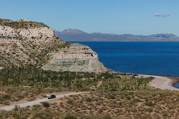 Four Wheel Camper truck on dirt road near coastal cliffs, off-grid boondocking overlanding adventure.