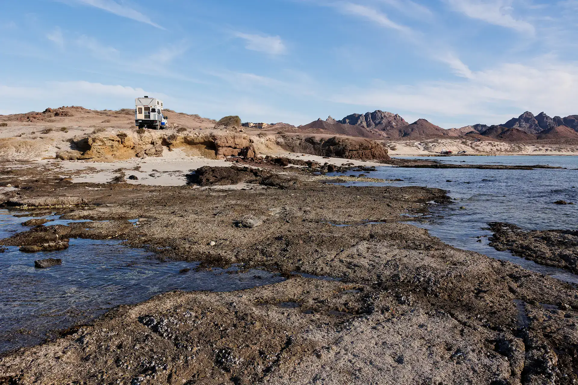 Four Wheel Camper parked for boondocking off-grid overlooking rocky coastline and ocean, desert mountains backdrop.