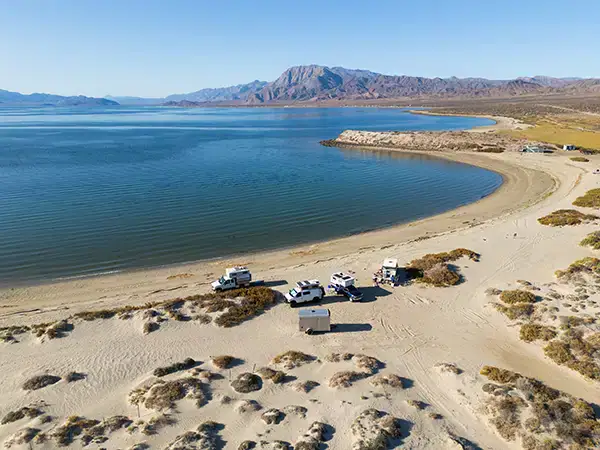 Four Wheel Camper vehicles boondocking off-grid by tranquil bay, overlanding adventure.