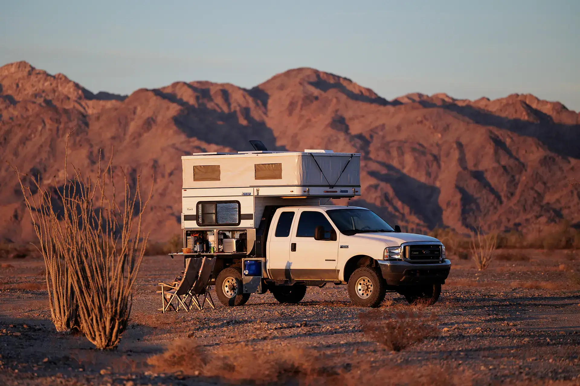 Four Wheel Camper truck setup boondocking off-grid with chairs and table deployed.