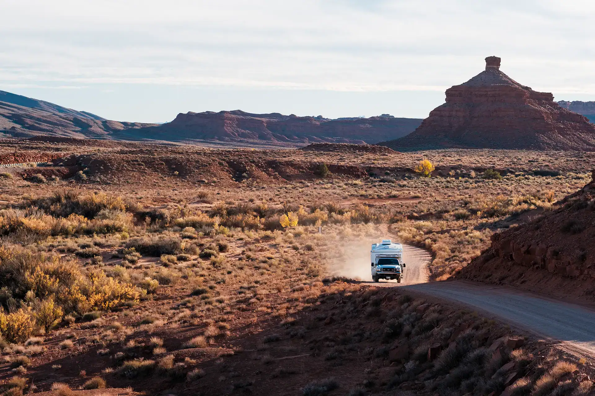 Four Wheel Camper driving dusty road, boondocking off-grid overlanding through desert landscape with rock formations.