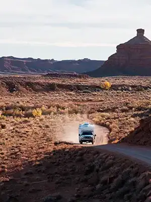 Four Wheel Camper off-grid boondocking on dusty road, overlanding through desert landscape.
