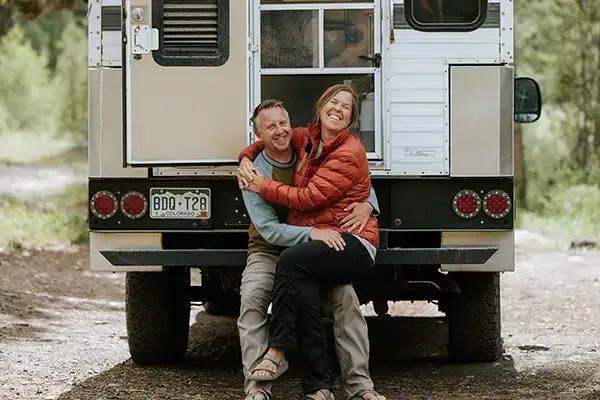 Happy couple embraces in front of Four Wheel Camper, boondocking off-grid overlanding adventure