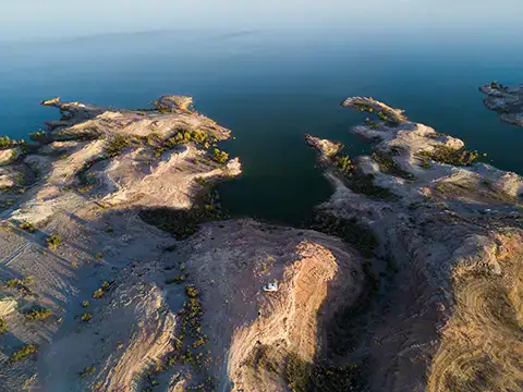 Four Wheel Camper boondocking off-grid, overlanding rocky desert landscape beside serene blue water.
