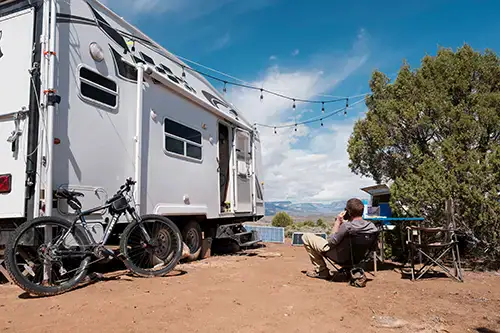 Fifth wheel camper, bicycle, person sitting, boondocking, off-grid, overlanding setup.