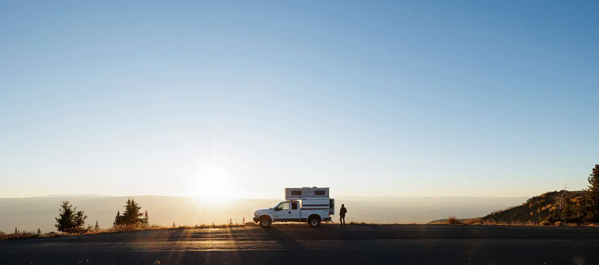 Four Wheel Camper on truck, person standing near, boondocking off-grid, overlanding adventure landscape.