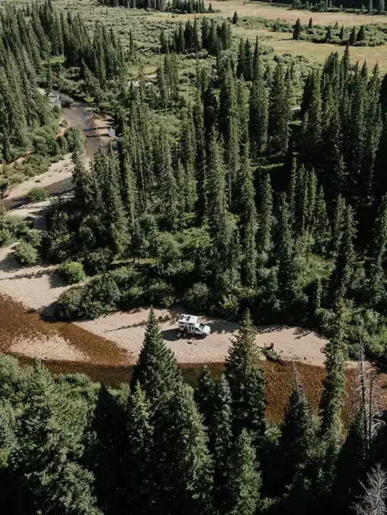Four Wheel Camper parked for boondocking off-grid overlanding beside forest stream.