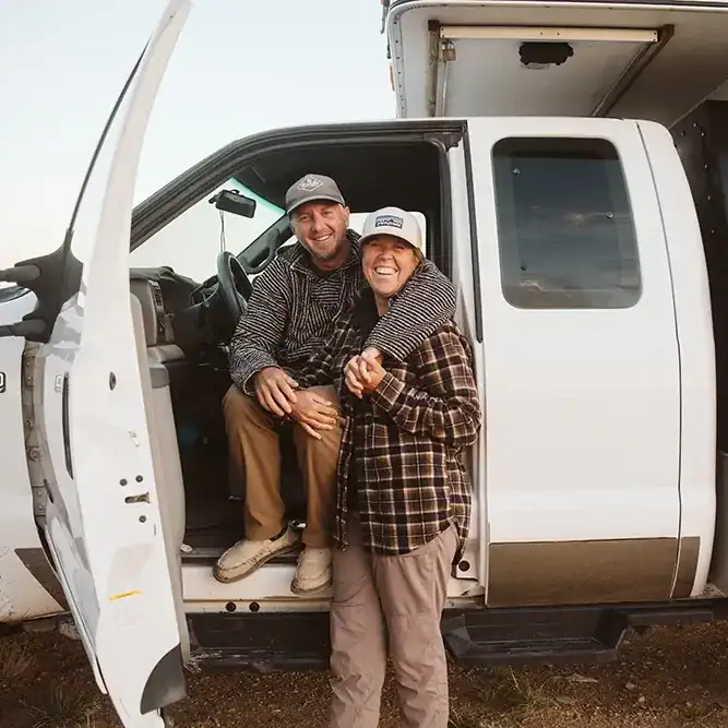 Couple smiles by Four Wheel Camper truck, ready for boondocking and overlanding off-grid adventures.